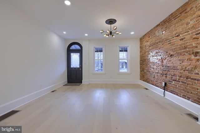 foyer entrance with light hardwood / wood-style floors, a chandelier, and brick wall