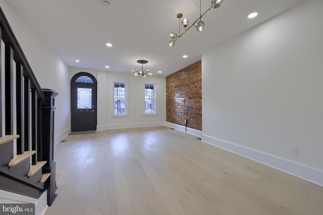 foyer entrance featuring a notable chandelier, light hardwood / wood-style flooring, and brick wall