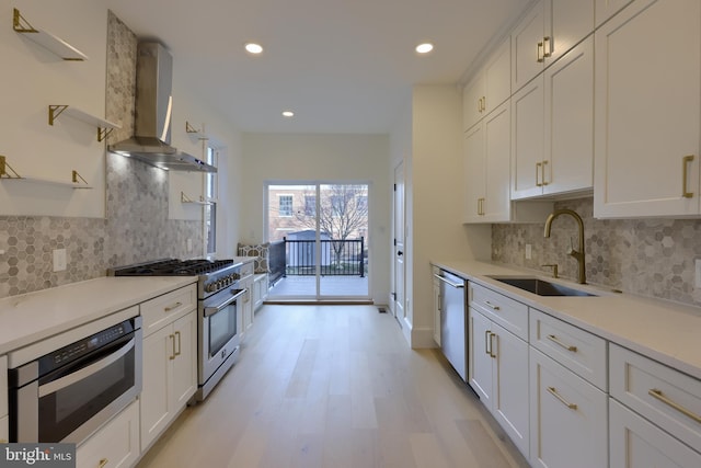 kitchen featuring sink, light hardwood / wood-style flooring, appliances with stainless steel finishes, white cabinetry, and wall chimney exhaust hood