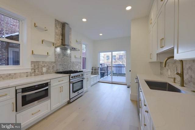 kitchen with wall chimney exhaust hood, sink, light stone counters, stainless steel appliances, and white cabinets