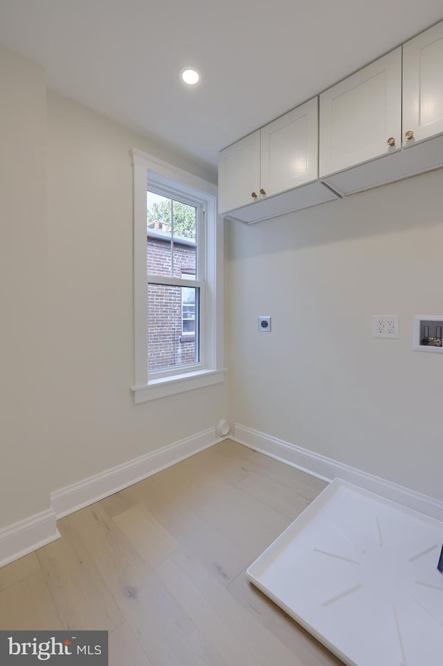 clothes washing area featuring cabinets, light hardwood / wood-style floors, hookup for a washing machine, and electric dryer hookup