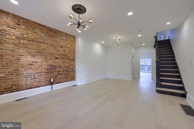 empty room featuring a notable chandelier, light hardwood / wood-style flooring, and brick wall