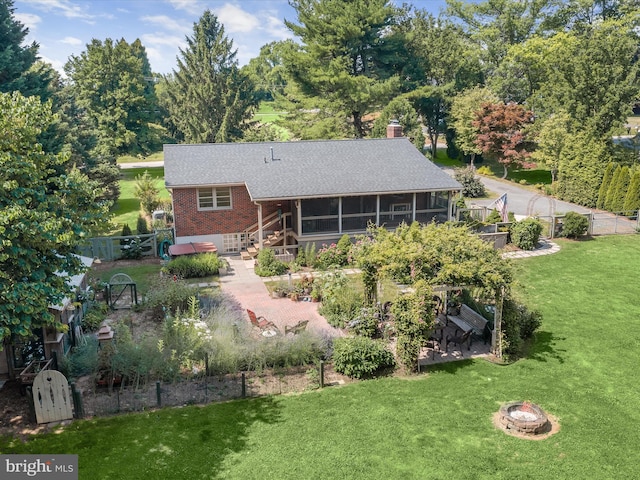 back of property with a sunroom, a yard, and a fire pit