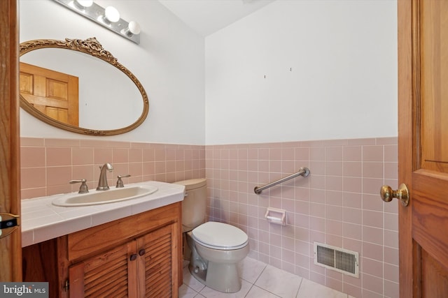 half bath featuring toilet, vanity, tile walls, tile patterned floors, and wainscoting