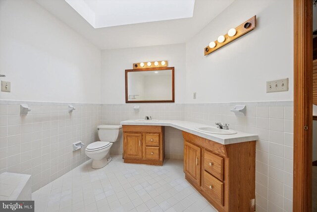 full bath with tile walls, a skylight, tile patterned flooring, wainscoting, and toilet