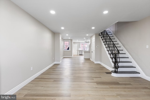 unfurnished living room featuring an inviting chandelier and light hardwood / wood-style flooring