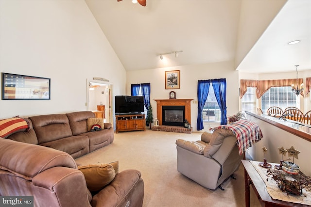 living room with carpet, ceiling fan with notable chandelier, a fireplace, and high vaulted ceiling