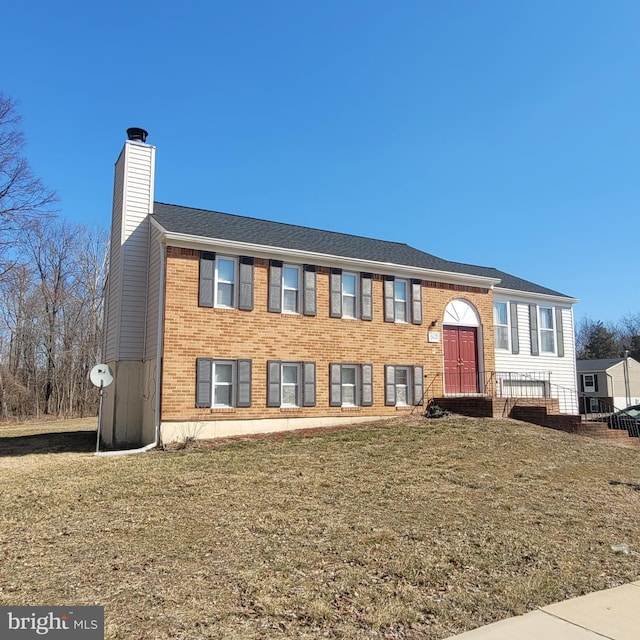 raised ranch featuring a front yard, brick siding, and a chimney