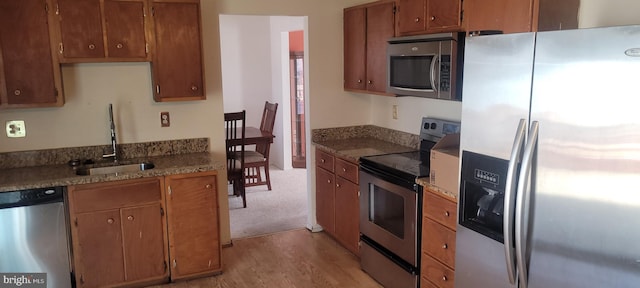 kitchen with brown cabinets, light wood-type flooring, stainless steel appliances, and a sink