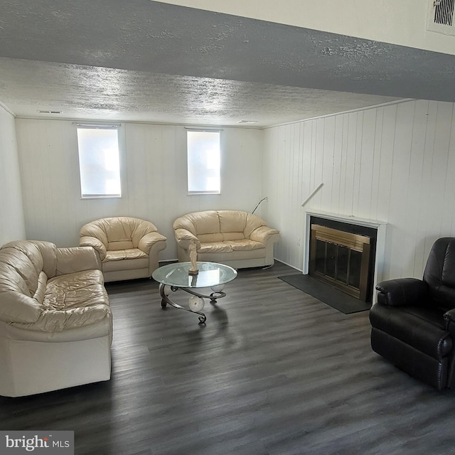 living room featuring a glass covered fireplace, visible vents, a textured ceiling, and wood finished floors