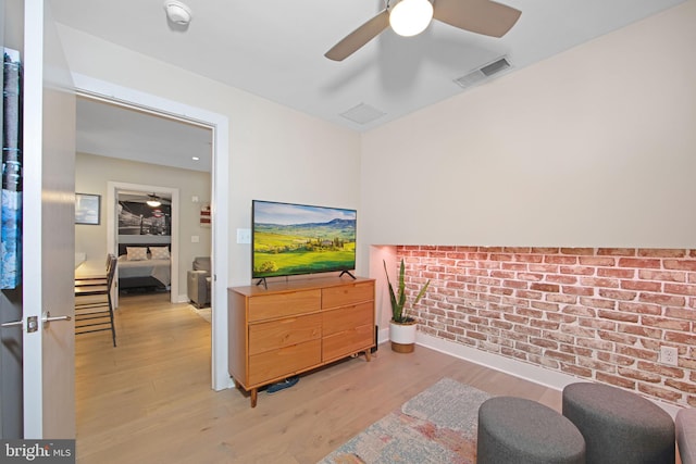 living area featuring light hardwood / wood-style floors, ceiling fan, and brick wall