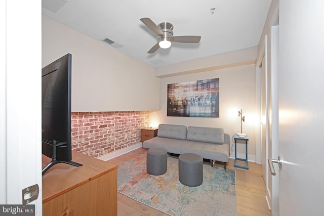 living room featuring light hardwood / wood-style flooring, ceiling fan, and brick wall