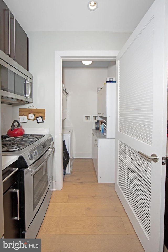 kitchen with stainless steel appliances, stacked washer / dryer, dark brown cabinets, and light hardwood / wood-style flooring