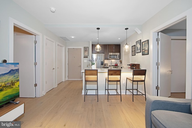 kitchen with light hardwood / wood-style flooring, a breakfast bar, dark brown cabinets, stainless steel appliances, and kitchen peninsula