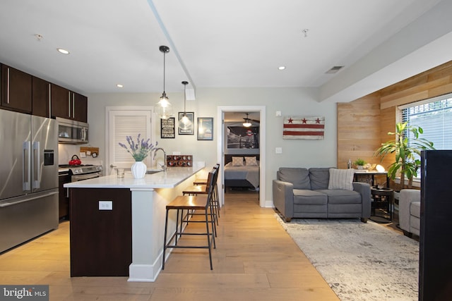 kitchen with dark brown cabinets, a kitchen breakfast bar, an island with sink, pendant lighting, and stainless steel appliances