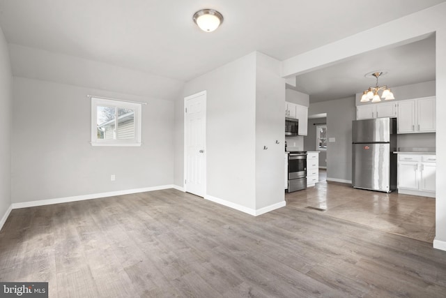 unfurnished living room with a notable chandelier, wood finished floors, and baseboards