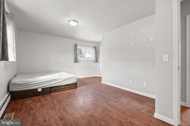 unfurnished bedroom with a baseboard heating unit, wood finished floors, and baseboards