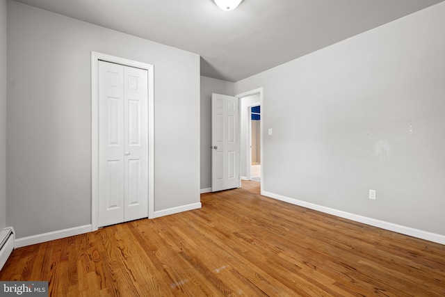 unfurnished bedroom with a baseboard heating unit, wood finished floors, baseboards, and a closet