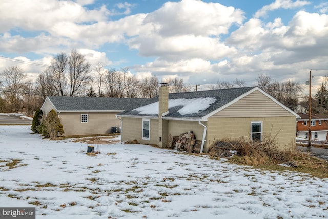 snow covered back of property featuring a chimney and a shingled roof