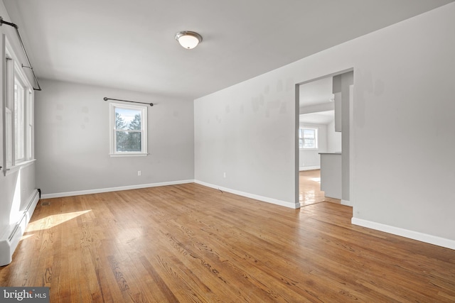 spare room with baseboard heating, light wood-style flooring, and baseboards