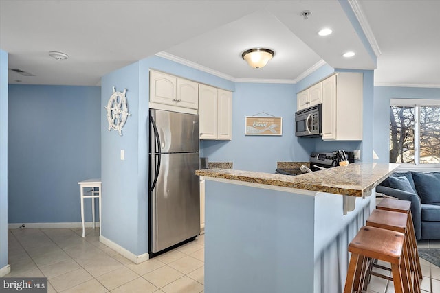 kitchen with appliances with stainless steel finishes, white cabinets, a kitchen breakfast bar, ornamental molding, and kitchen peninsula