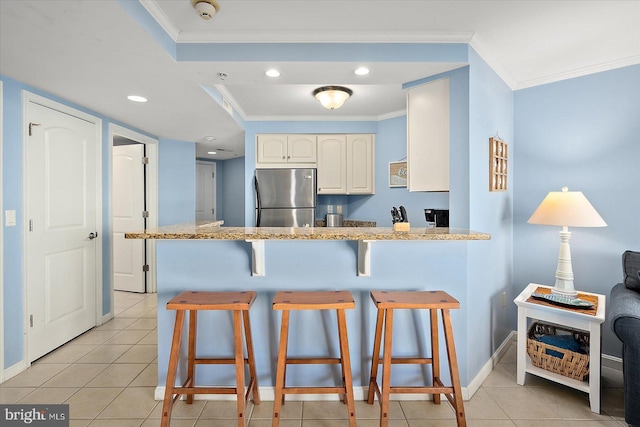 kitchen featuring light stone counters, ornamental molding, stainless steel fridge, and kitchen peninsula