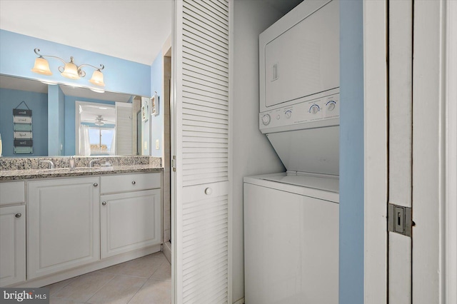 clothes washing area with stacked washer / drying machine, light tile patterned floors, and sink