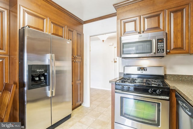 kitchen featuring crown molding, appliances with stainless steel finishes, dark stone counters, and light tile patterned floors