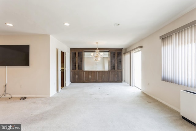 unfurnished living room with a notable chandelier, light colored carpet, and radiator