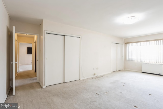 unfurnished bedroom with light colored carpet, radiator, and two closets