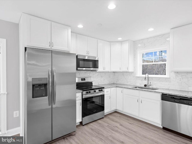 kitchen with light stone countertops, white cabinetry, appliances with stainless steel finishes, and sink