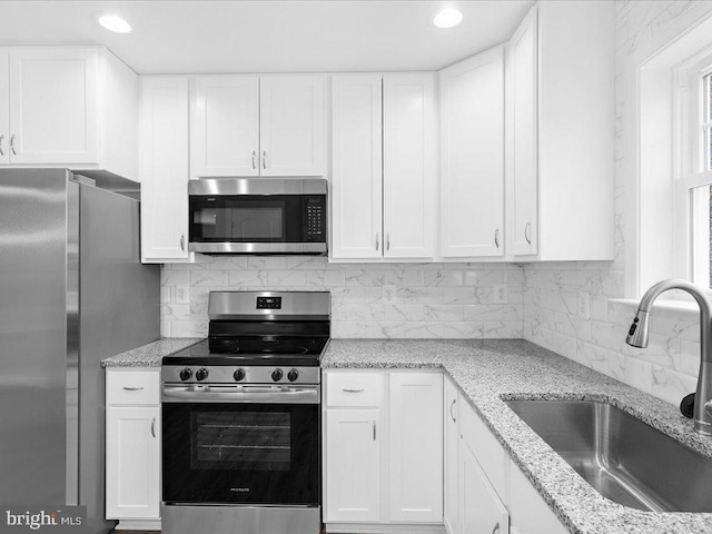 kitchen with stainless steel appliances, white cabinetry, sink, and tasteful backsplash