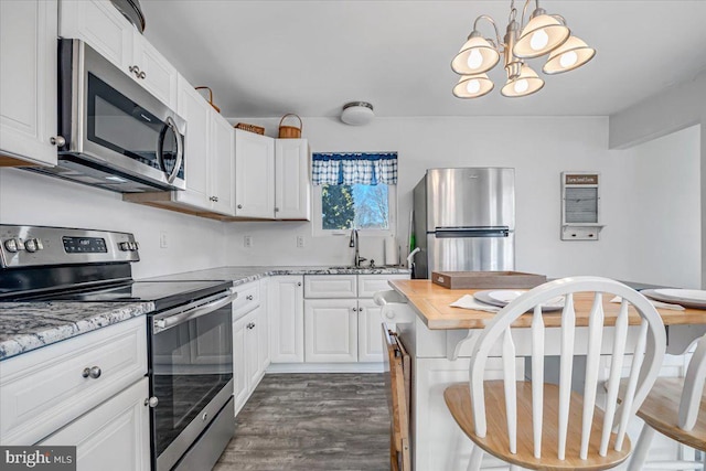 kitchen with sink, white cabinets, dark hardwood / wood-style flooring, hanging light fixtures, and stainless steel appliances