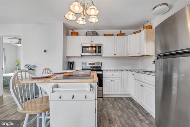 kitchen featuring decorative light fixtures, wood-type flooring, a breakfast bar area, white cabinets, and stainless steel appliances