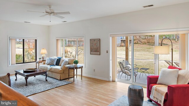 living room featuring a ceiling fan, visible vents, light wood-style flooring, and baseboards