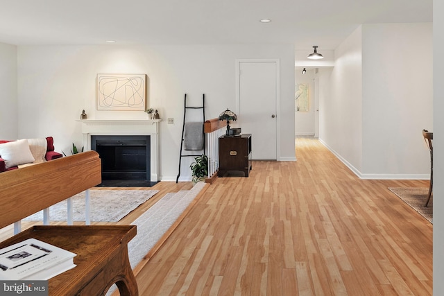 living area with light wood-style floors, recessed lighting, baseboards, and a fireplace with flush hearth