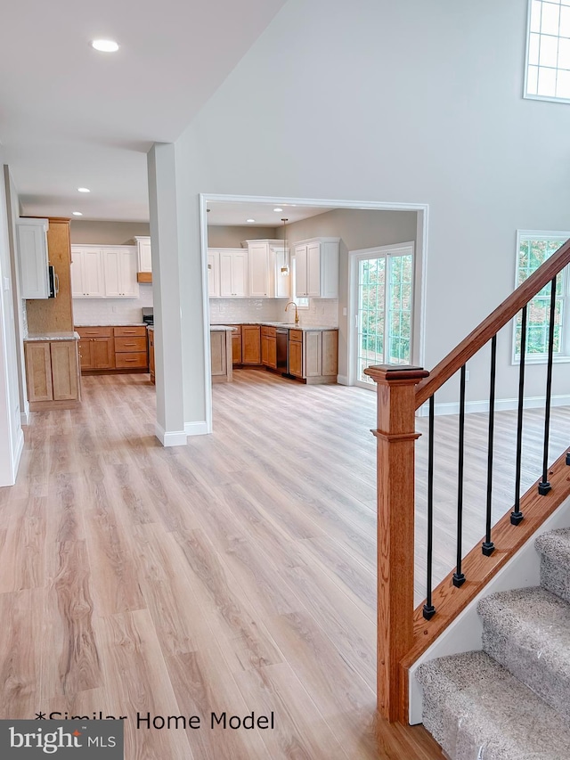 unfurnished living room featuring a towering ceiling, sink, and light hardwood / wood-style flooring