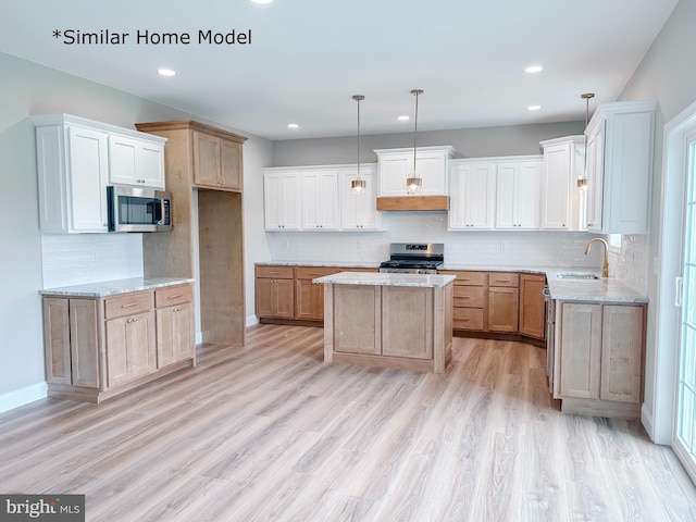 kitchen with sink, hanging light fixtures, appliances with stainless steel finishes, a kitchen island, and light hardwood / wood-style floors