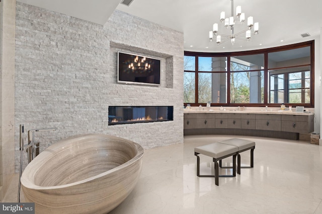 bathroom featuring vanity, a washtub, a stone fireplace, and an inviting chandelier