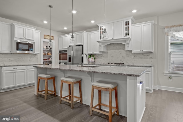 kitchen with stainless steel appliances, light stone countertops, a kitchen island with sink, and decorative light fixtures