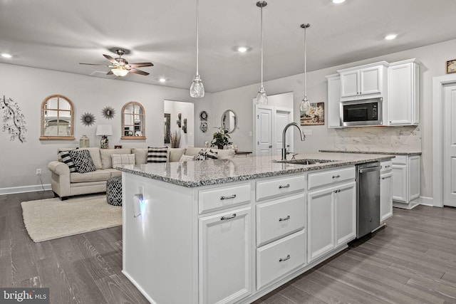 kitchen featuring decorative light fixtures, built in microwave, sink, white cabinets, and a kitchen island with sink