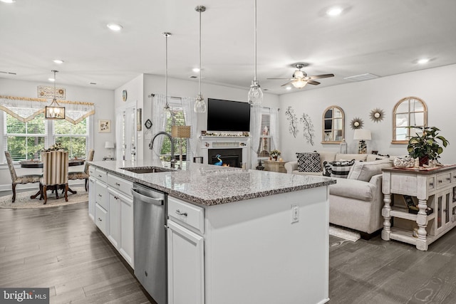 kitchen with sink, white cabinets, hanging light fixtures, light stone countertops, and a center island with sink