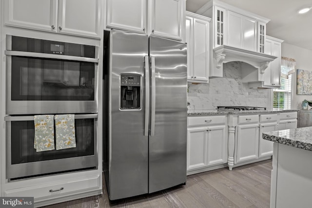 kitchen featuring appliances with stainless steel finishes, white cabinets, light stone counters, and decorative backsplash