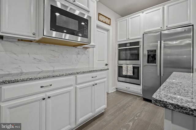 kitchen featuring white cabinetry, tasteful backsplash, light stone counters, stainless steel appliances, and hardwood / wood-style floors