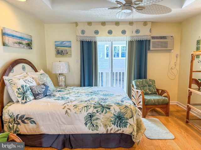 bedroom with ceiling fan, a wall mounted air conditioner, a textured ceiling, and light wood-type flooring