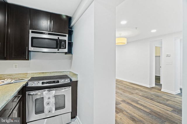 kitchen with light stone countertops, wood-type flooring, appliances with stainless steel finishes, and dark brown cabinets