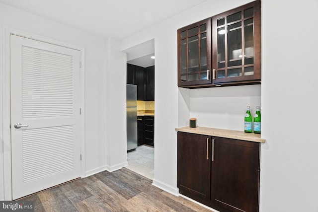 bar with hardwood / wood-style floors, dark brown cabinets, and stainless steel refrigerator