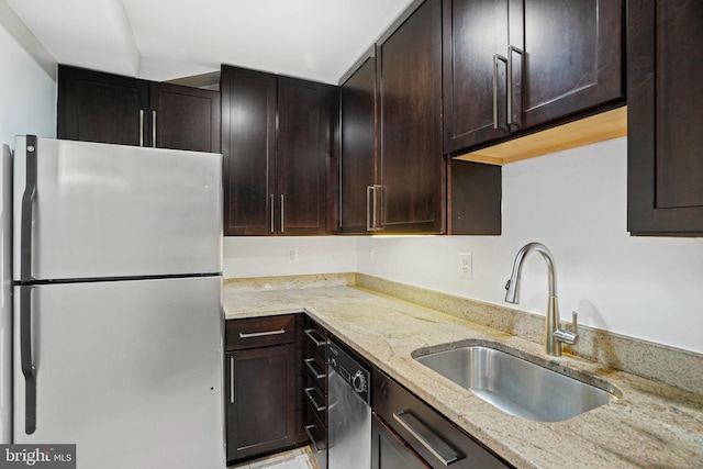 kitchen featuring sink, dishwashing machine, fridge, dark brown cabinetry, and light stone countertops