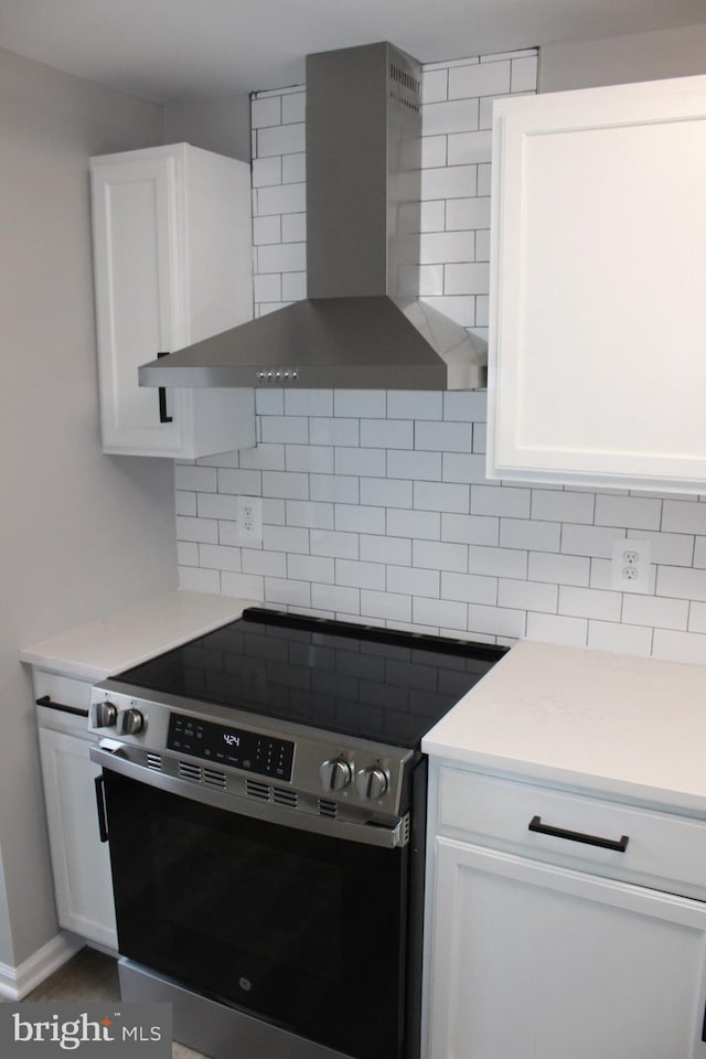 kitchen featuring white cabinets, electric range, wall chimney exhaust hood, and backsplash