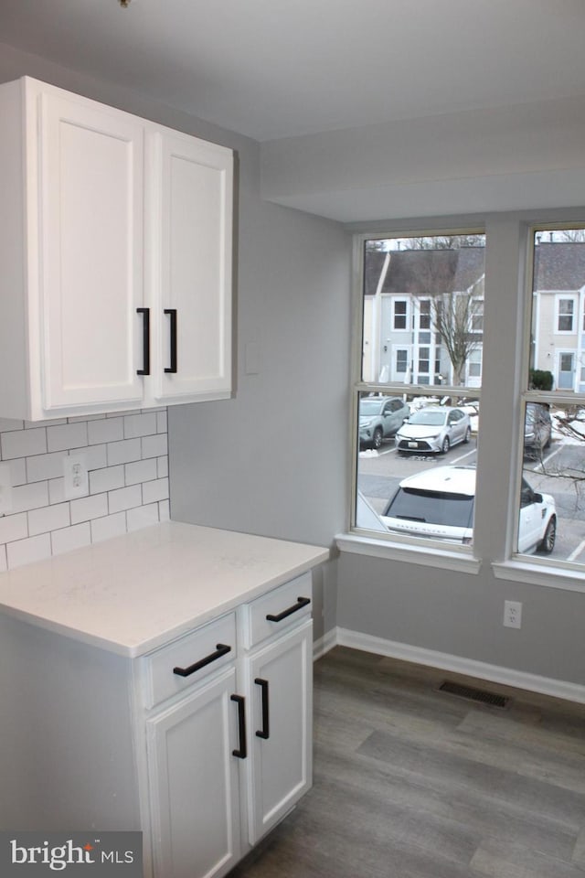 kitchen with dark wood-type flooring, light stone countertops, decorative backsplash, and white cabinets